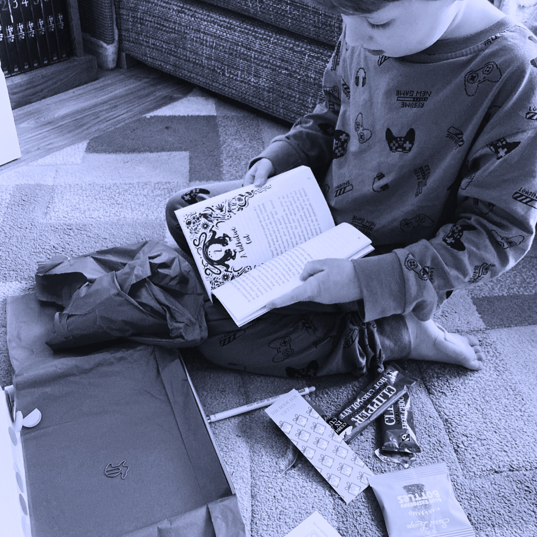 Child reading their new book from their monthly book subscription or one off book gift with additional treats and sweets.